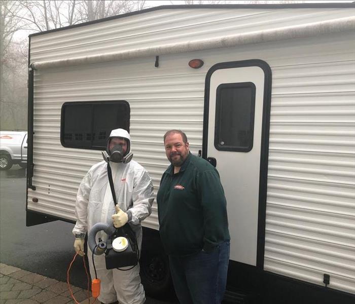 two SERVPRO persons, one in PPE, standing in front of a white travel trailer.