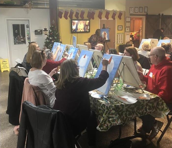 several people sitting around a table painting canvasses