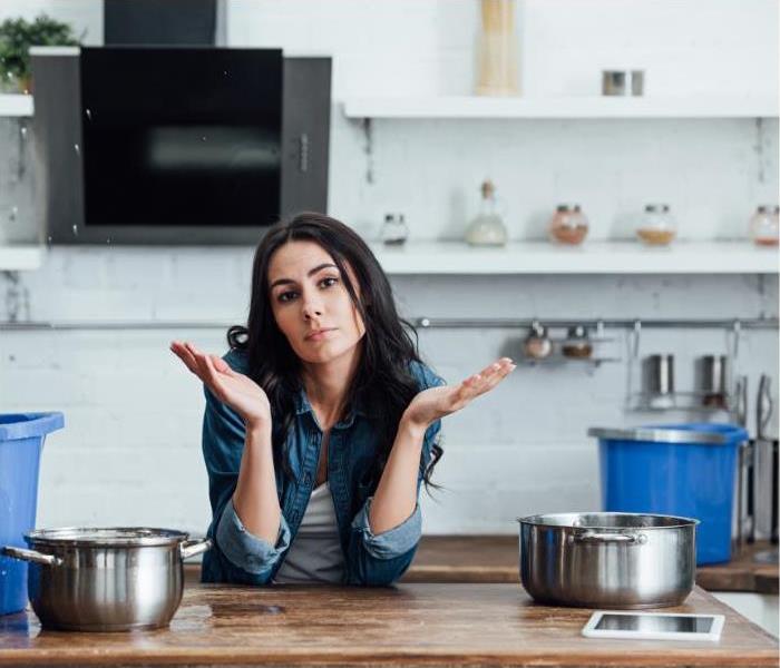 Brunette woman using pots and buckets during leak in kitchen